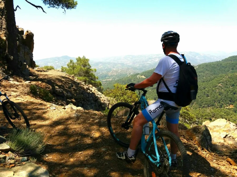 A mountain biker in Ramo kit stopped at a viewpoint above a deep wooded valley