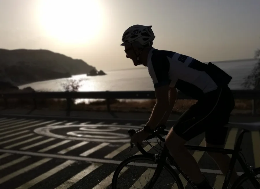 A rider in silhouette on a coast road, the low sun on the sea behind a rocky headland