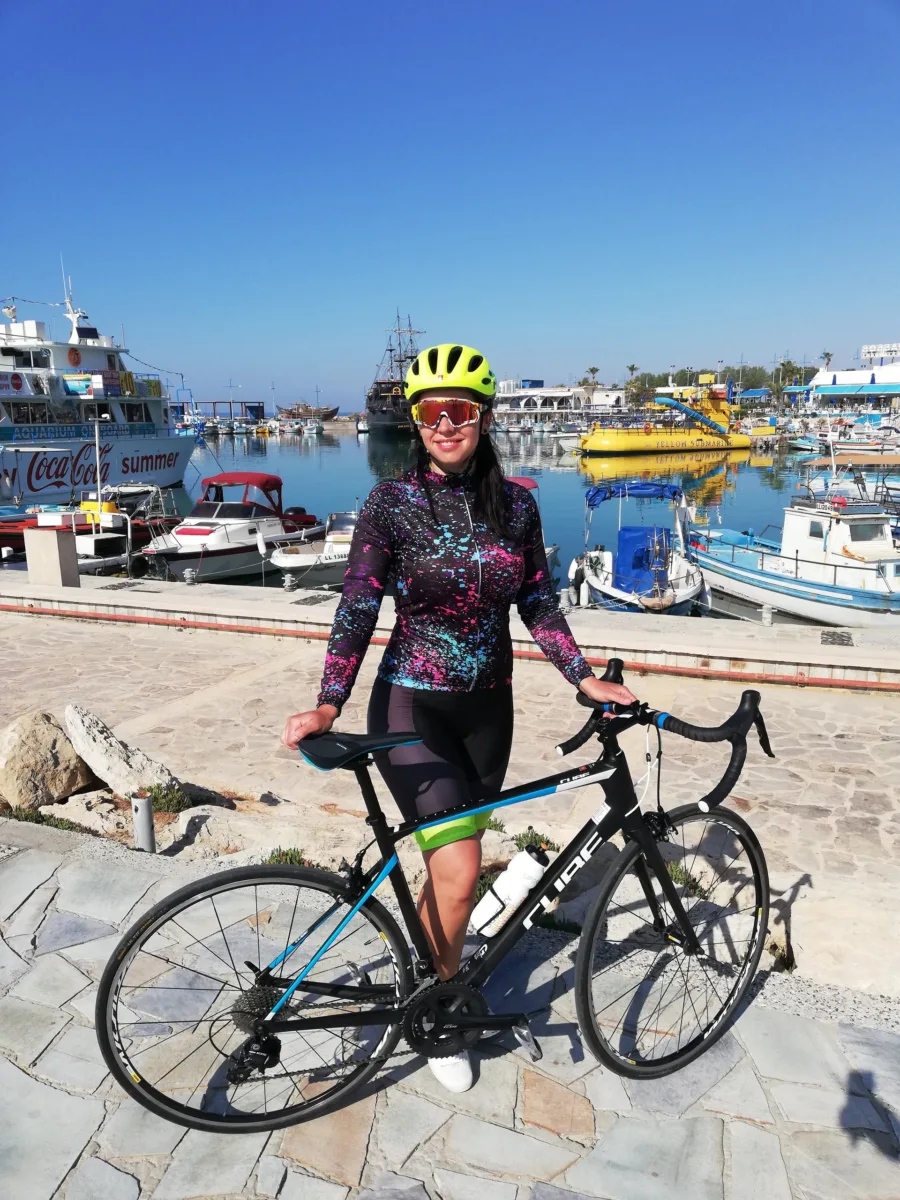 A rider standing with a road bike in front of a harbour full of fishing and tour boats