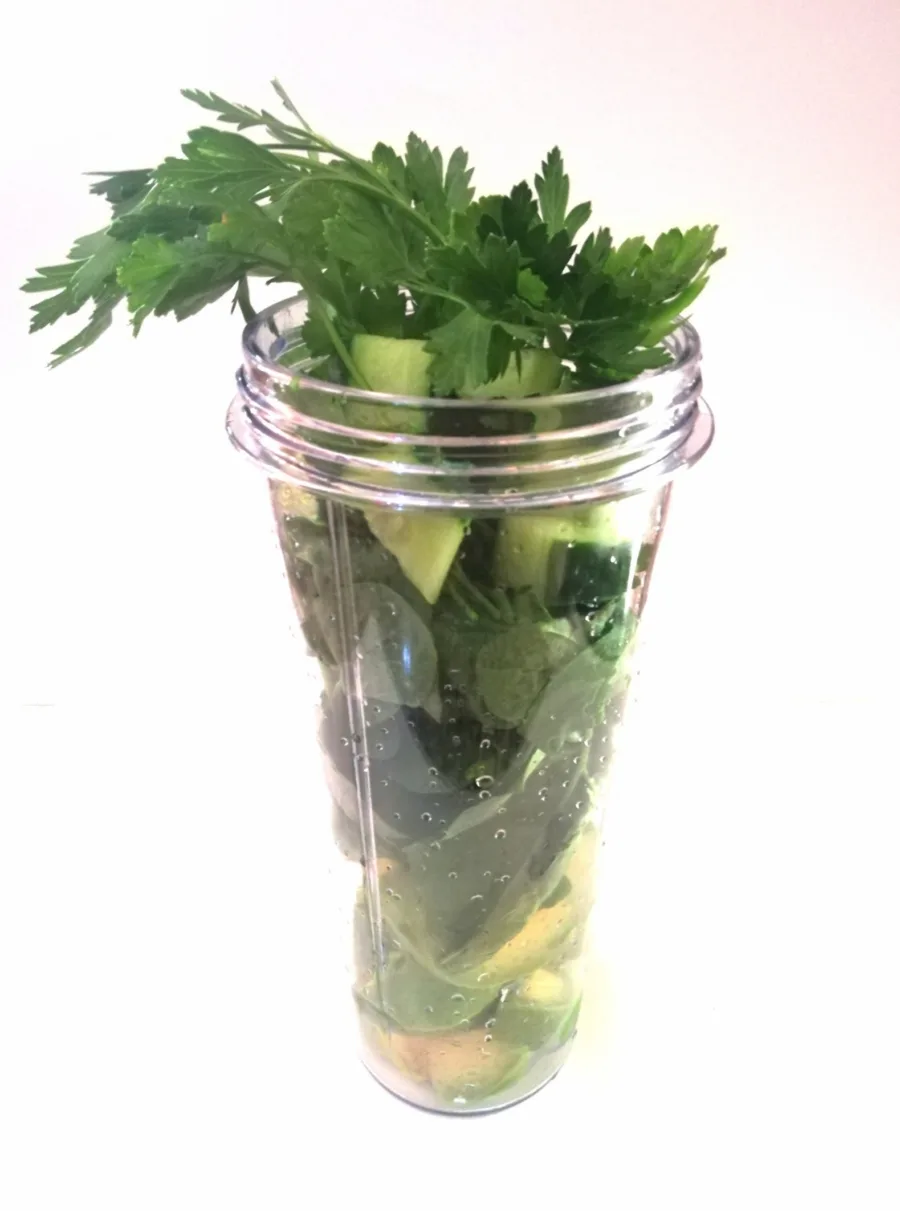 A blender cup packed with celery, cucumber and parsley before it is blended