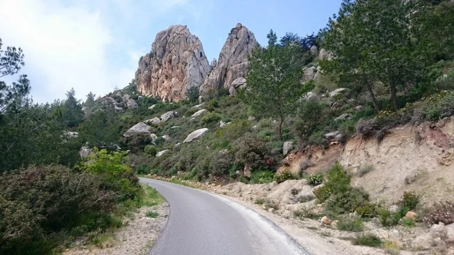 A narrow road bending under two tall granite outcrops on a scrubby hillside