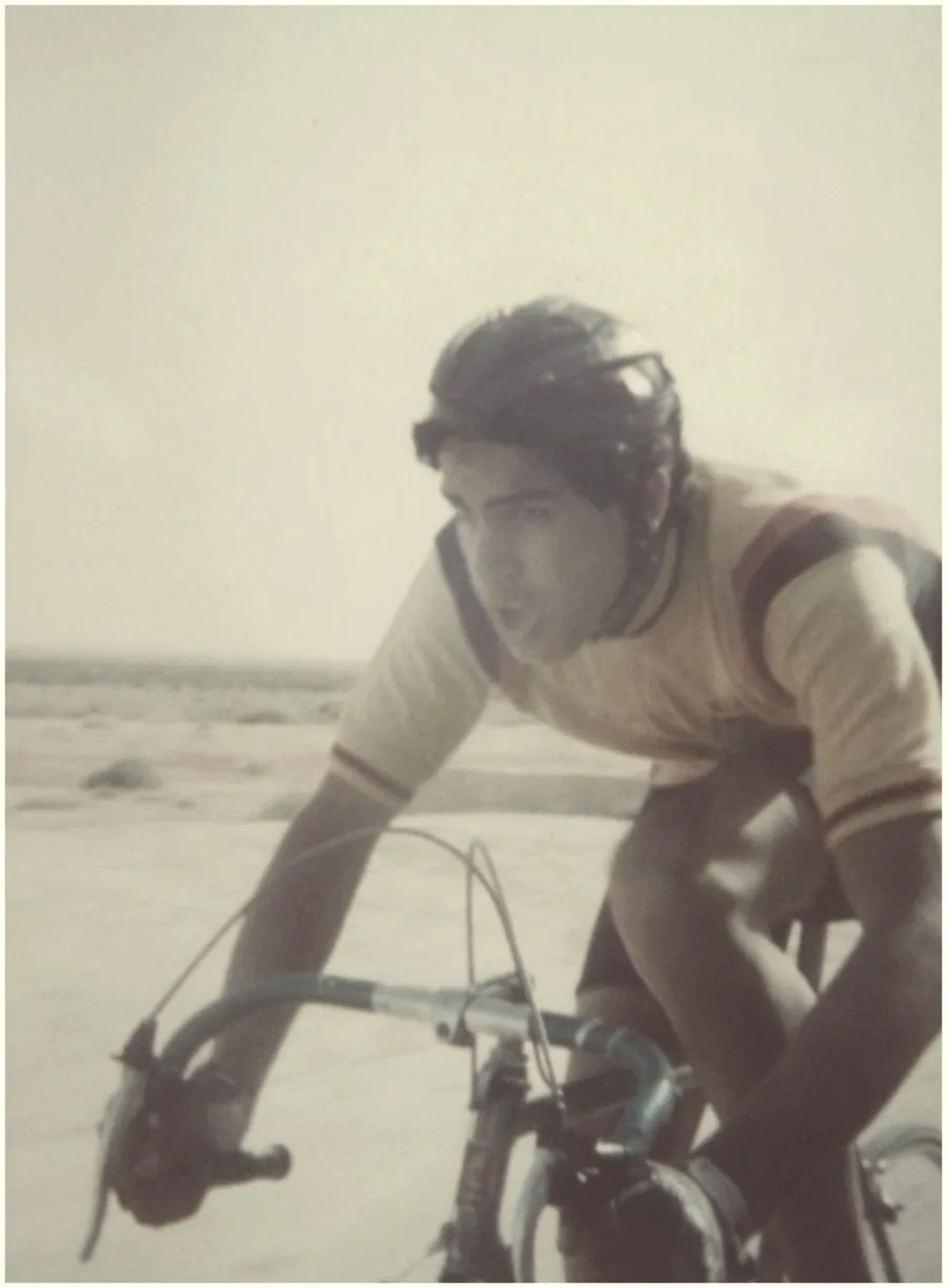 A faded photograph of a young rider on the drops of a steel road bike, wearing a leather hairnet helmet