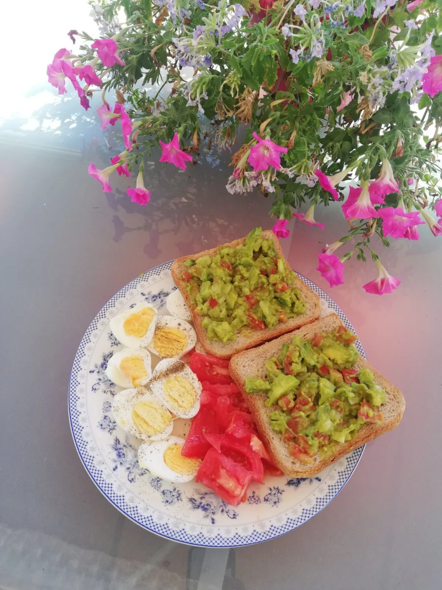 Avocado toast and boiled eggs on a plate beneath hanging flowers
