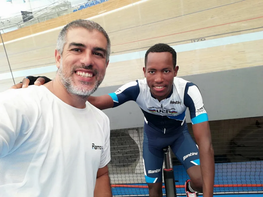Ramo and a rider in team kit at the trackside of an indoor velodrome