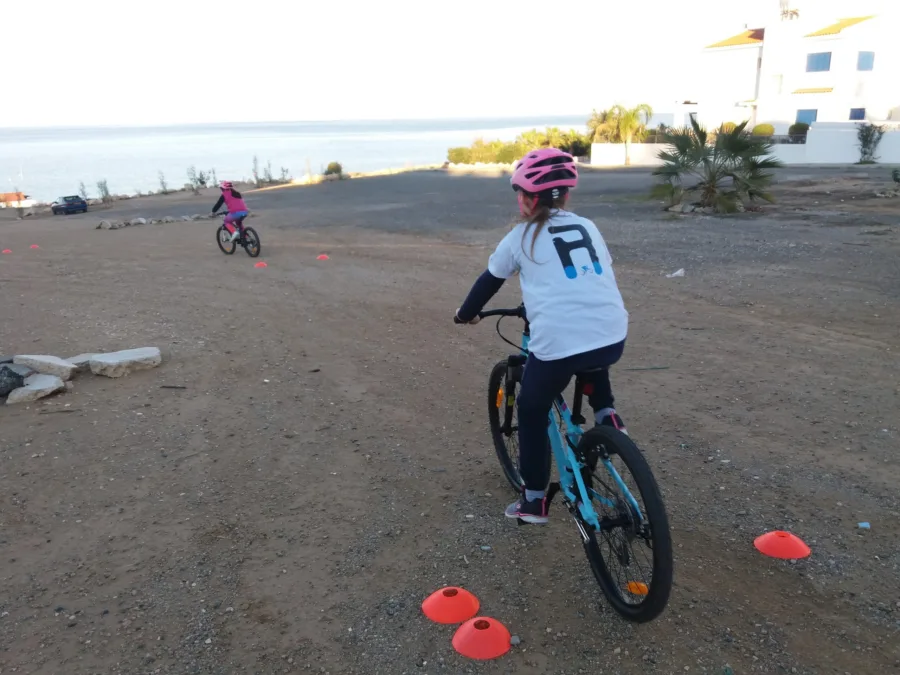 A child riding a mountain bike between cones on open ground by the sea