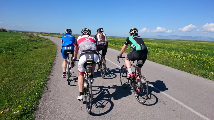 Four riders in club kit riding away across a flat green plain in spring