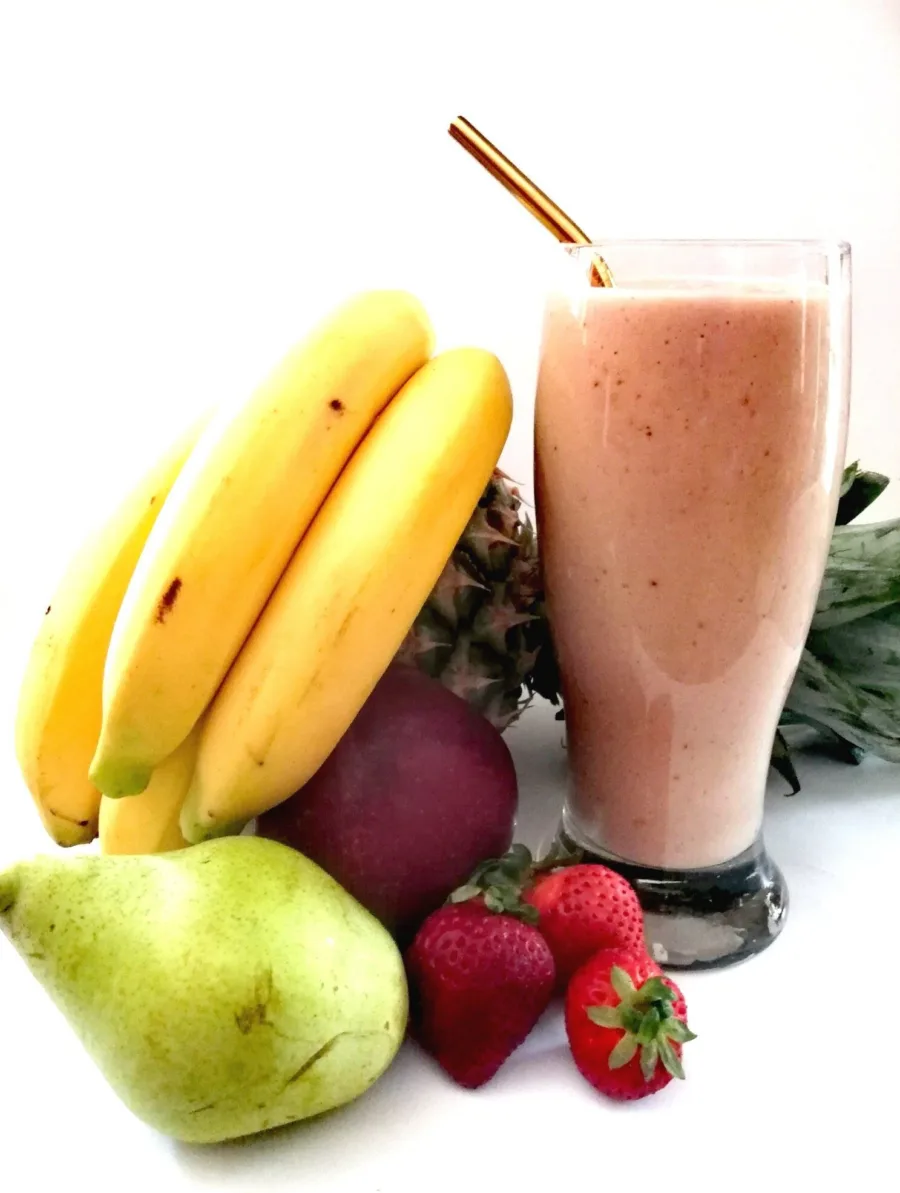 Bananas, a pear and strawberries beside a smoothie in a tall glass