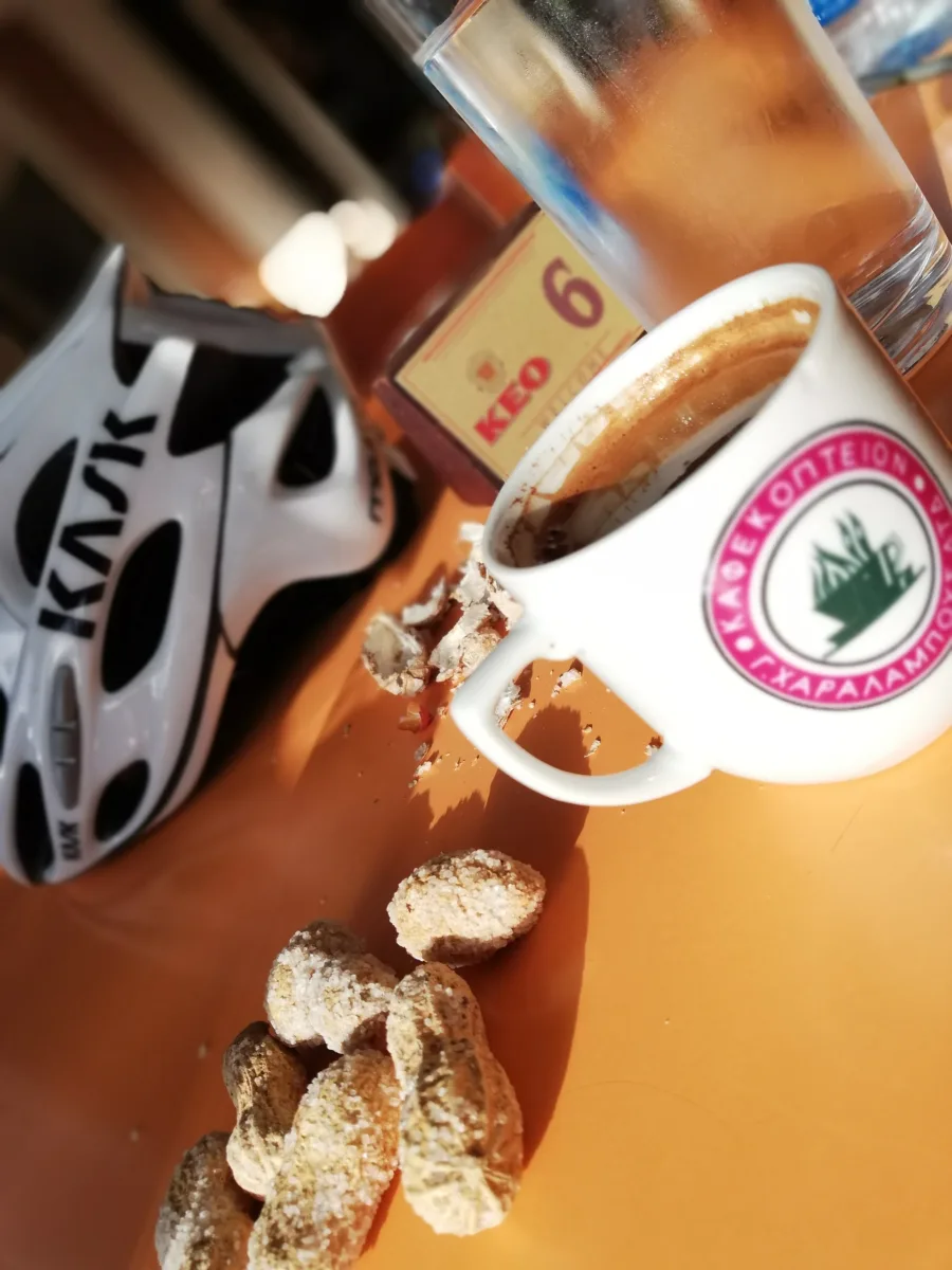 A cycling helmet on a cafe table beside a cup of Cypriot coffee, iced water and almond biscuits