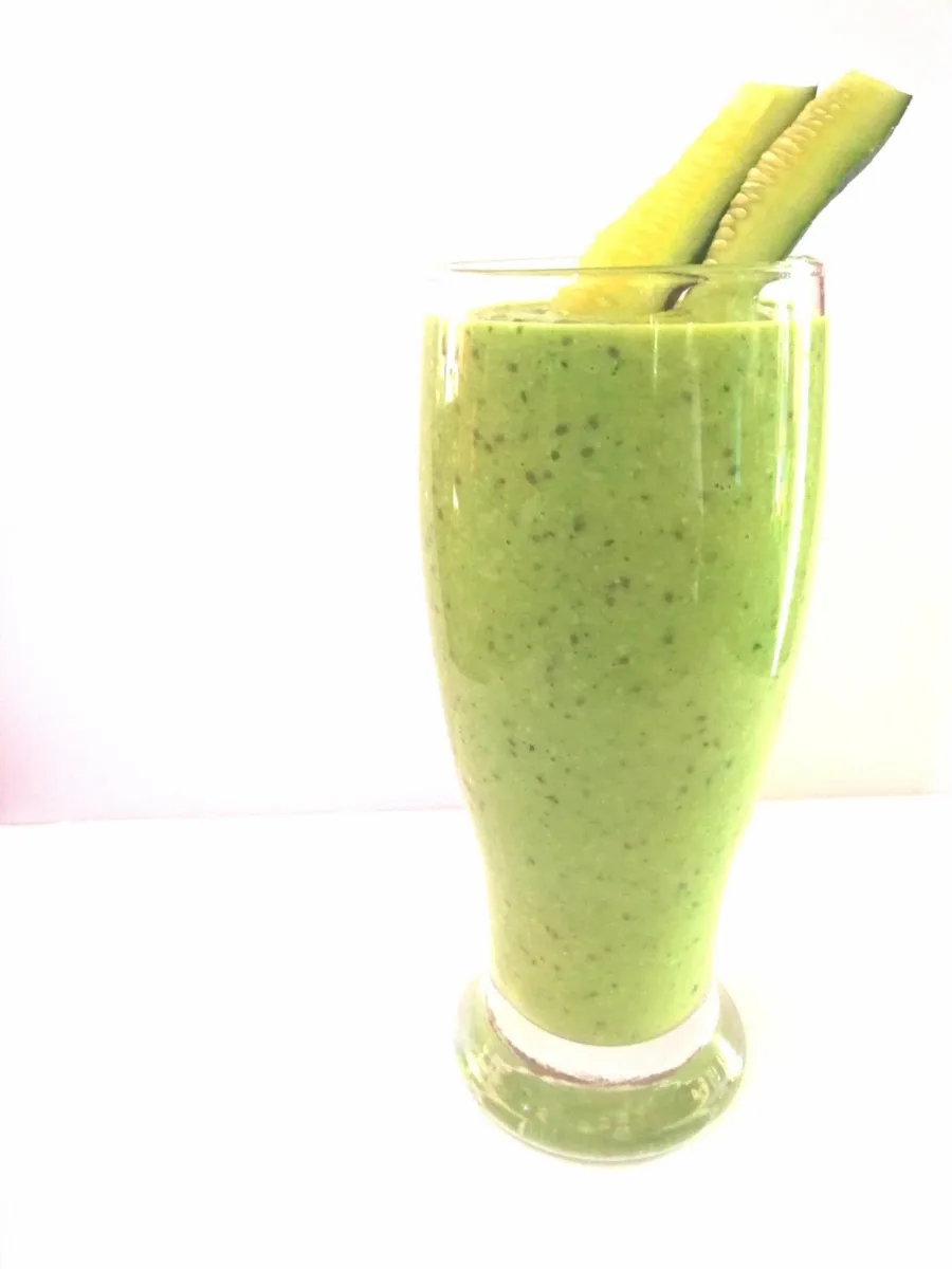 A green smoothie in a tall glass with two sticks of celery