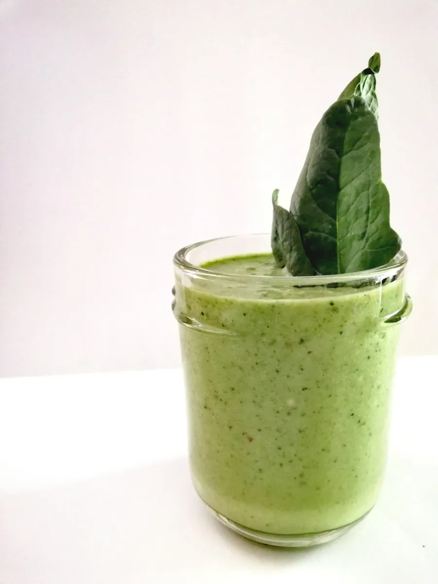 A glass of thick green smoothie with two spinach leaves standing up out of it