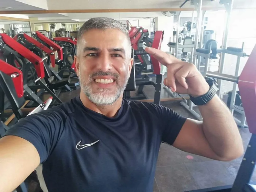 Ramo flexing one arm for the camera on a gym floor lined with red weight machines