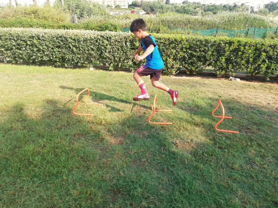 A boy jumping over a line of low agility hurdles set out on grass