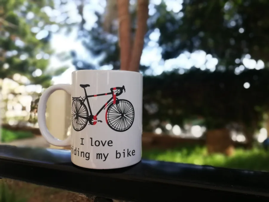A mug printed with a red and black road bike and the words I love riding my bike, on a balcony rail