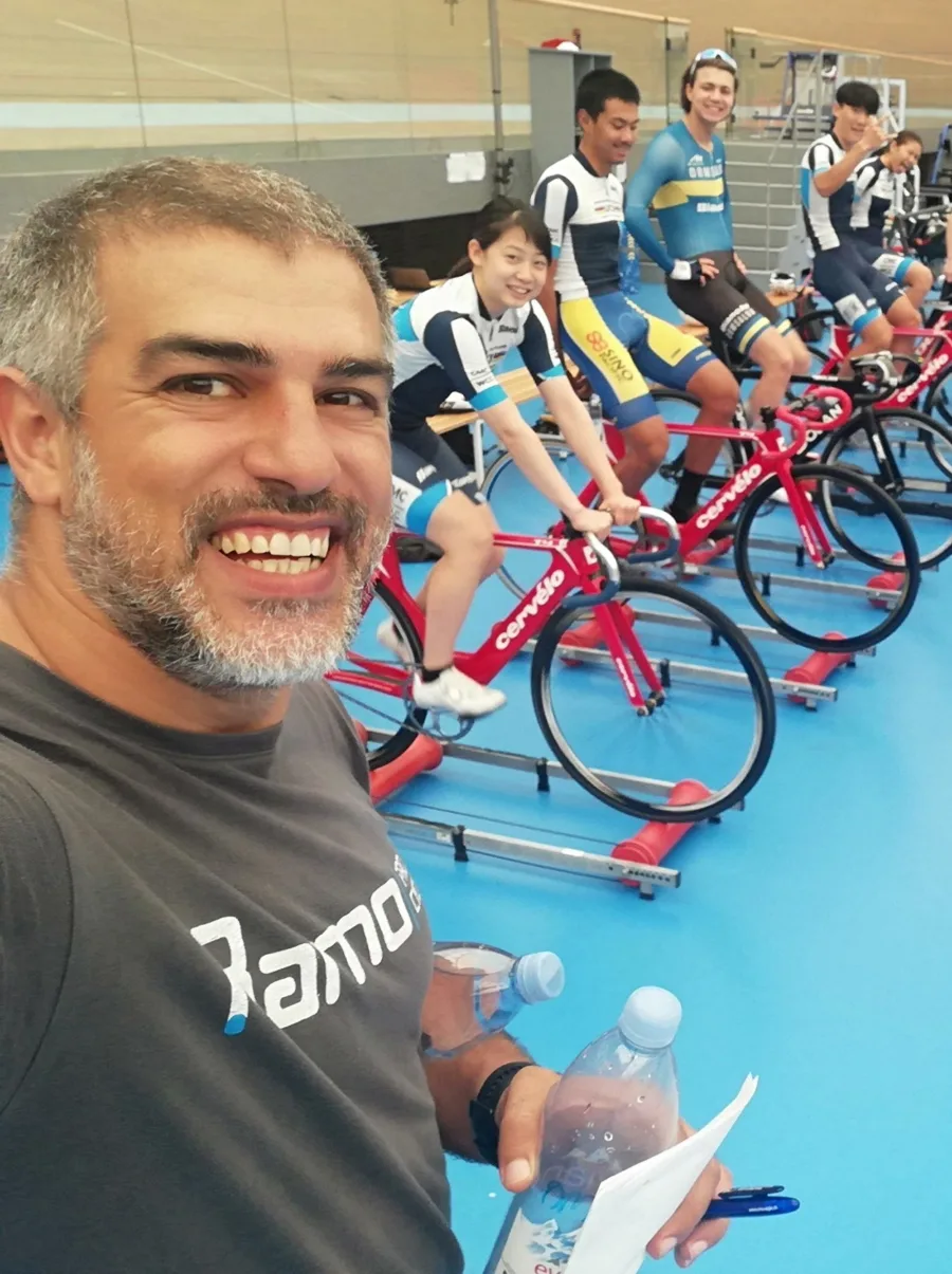 A coach takes a selfie in front of five riders warming up on rollers at the trackside