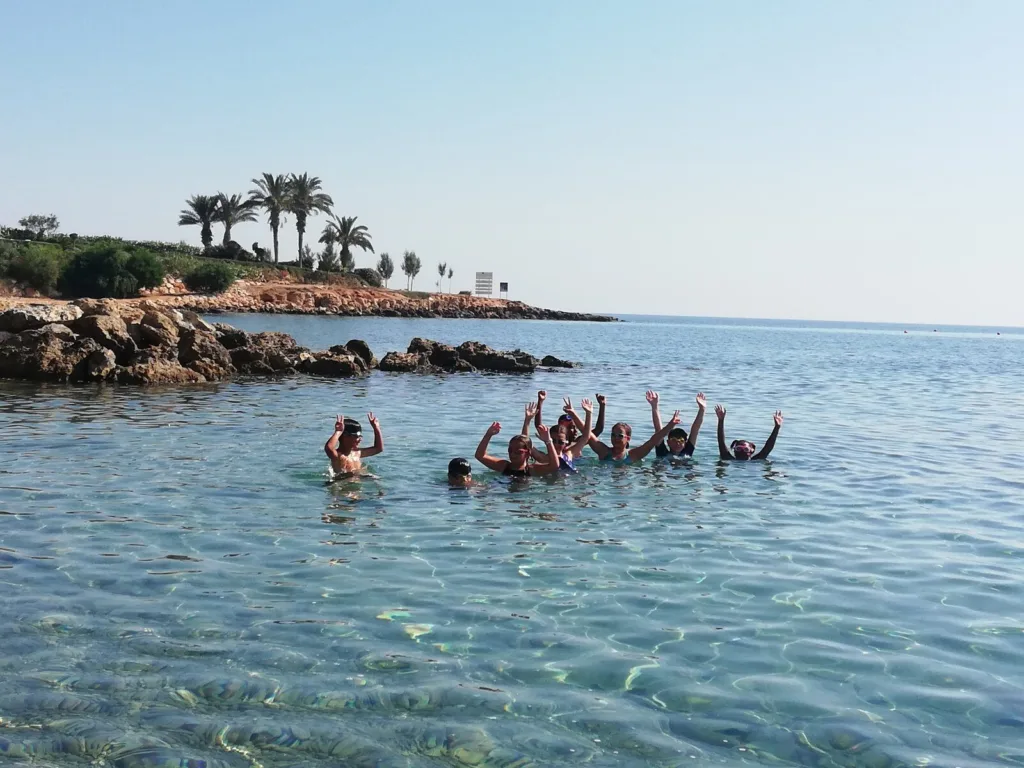 Swimmers gathered in clear shallow water beside a rocky headland