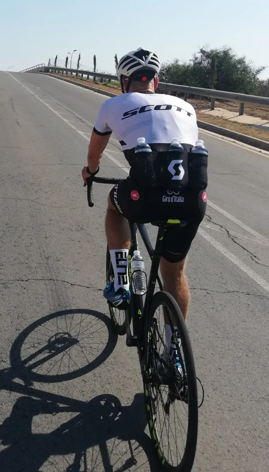 A rider from behind climbing onto a road bridge, three bottles in the jersey pockets