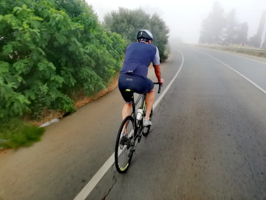 A rider seen from behind on a wet road disappearing into thick morning fog