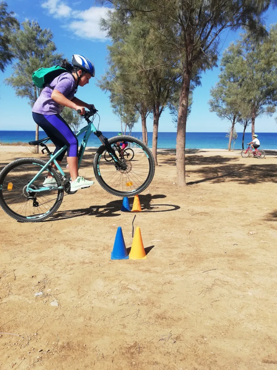 A child riding a mountain bike between marker cones on sand beside the sea