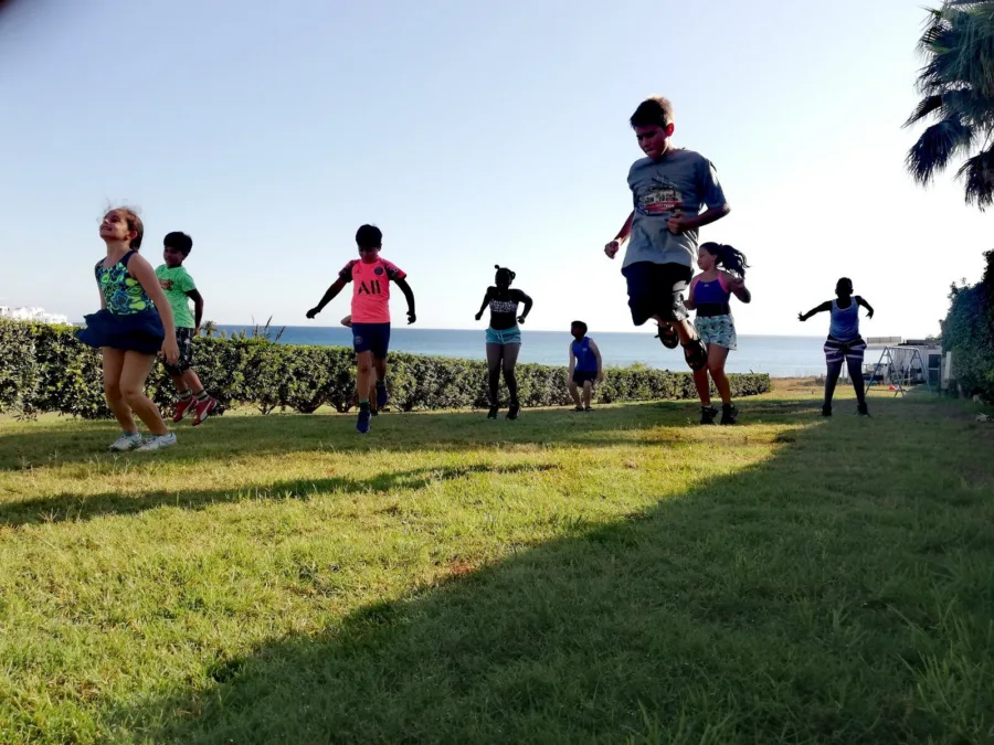 Children sprinting across a grass lawn towards the camera with the sea behind them