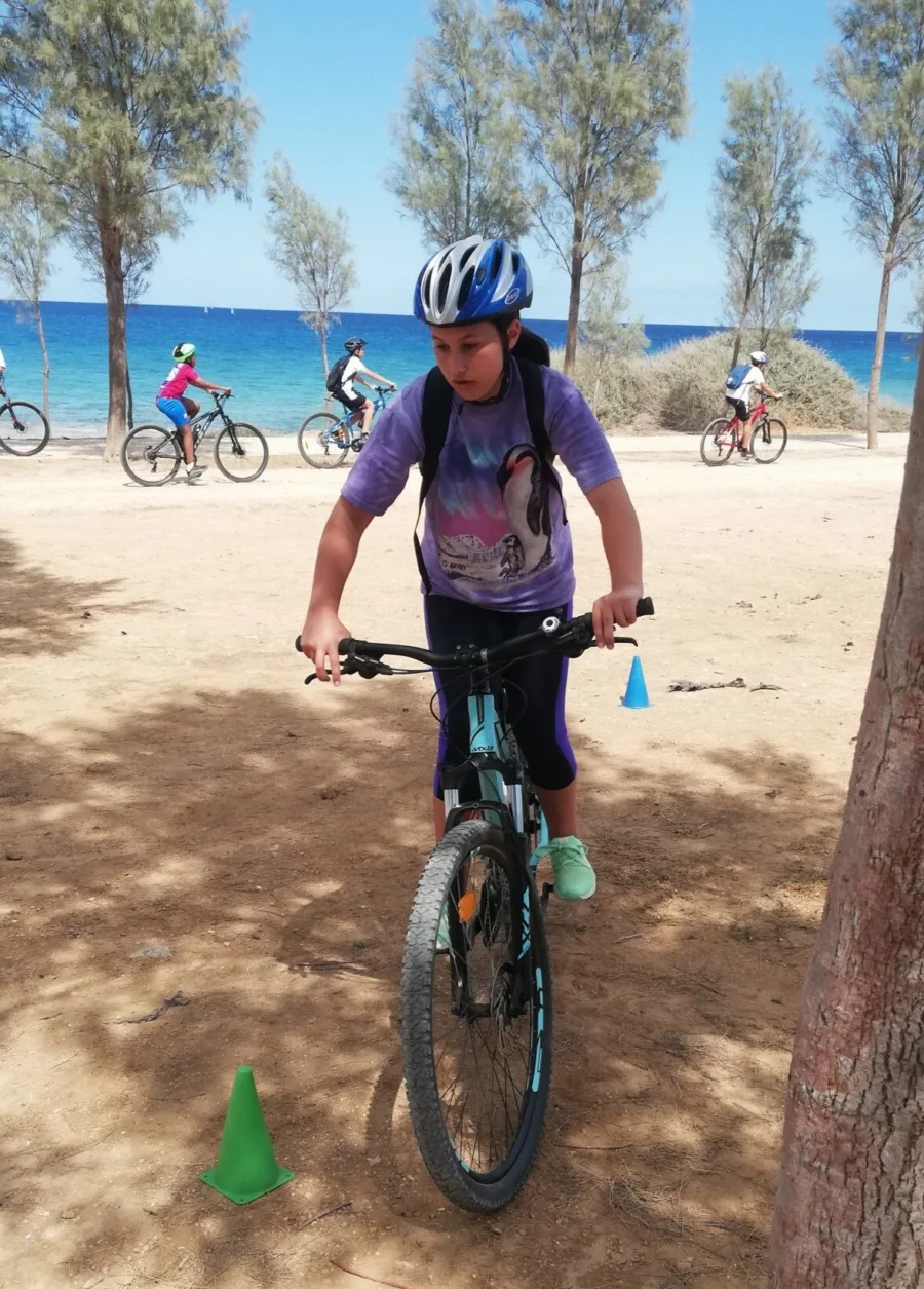 A child riding a mountain bike past a marker cone on a sandy track