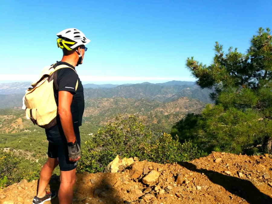 A rider with a rucksack standing on a red earth summit looking out over the hills