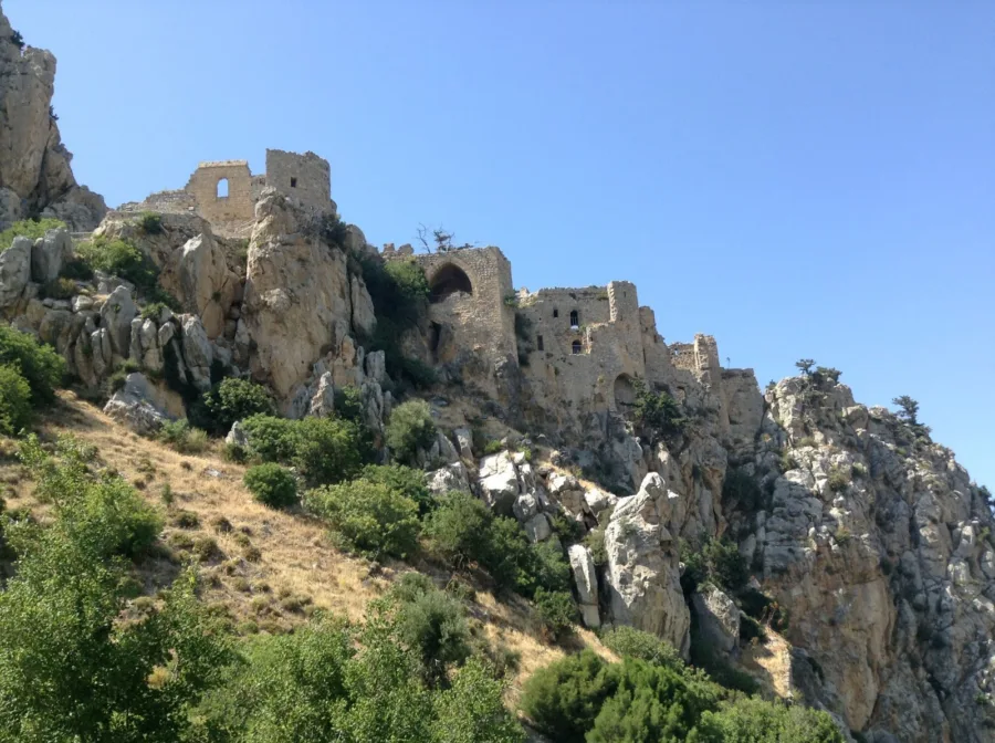 A ruined hilltop castle on jagged limestone crags against a clear blue sky