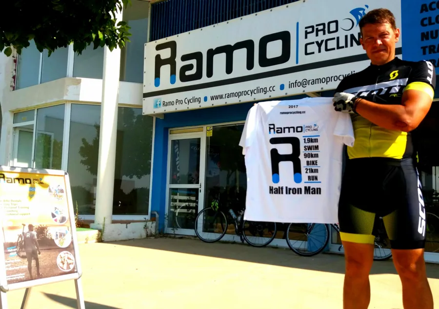 A rider outside the shop holding up a 2017 Ramo shirt printed 1.9 km swim, 90 km bike, 21 km run