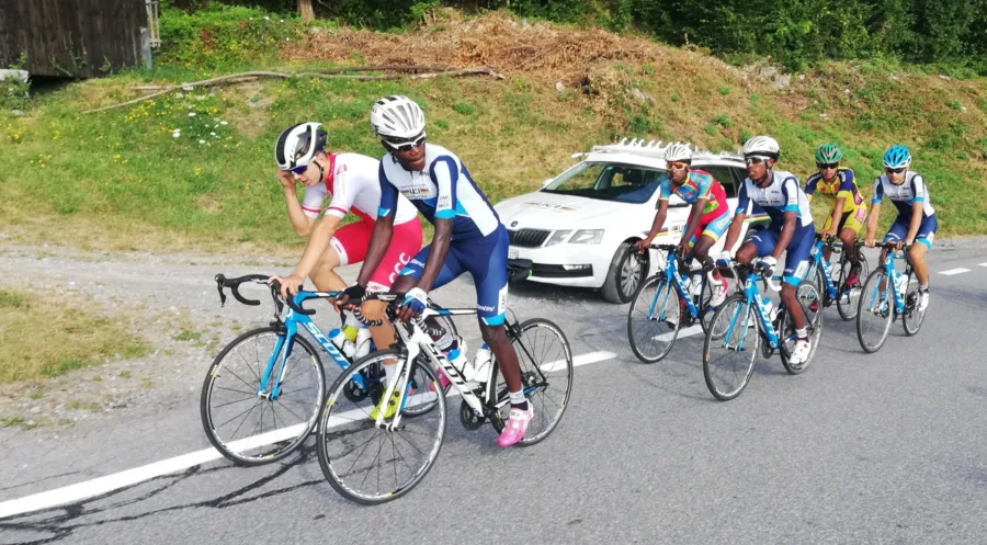 A small group of junior riders strung out on a road behind a following car
