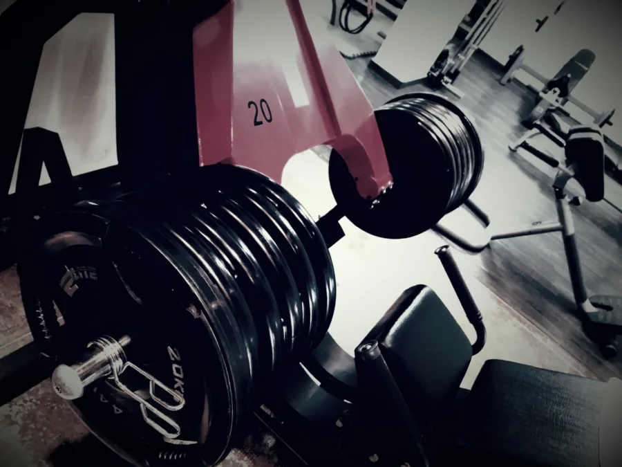 Loaded weight plates and a dumbbell in the foreground of an empty gym floor