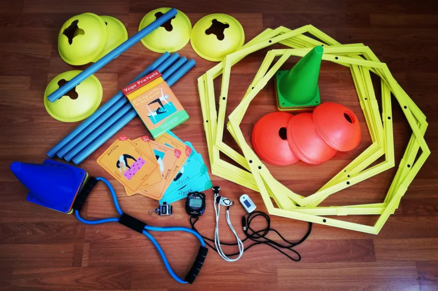 Coaching kit laid out on a wooden floor: agility hexagons, cones, poles, a resistance band, a stopwatch and skill cards