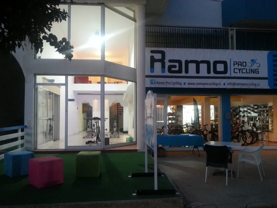 The Paralimni shop lit up at night, bikes and helmets on the wall inside and the spin studio glowing through the upstairs glass