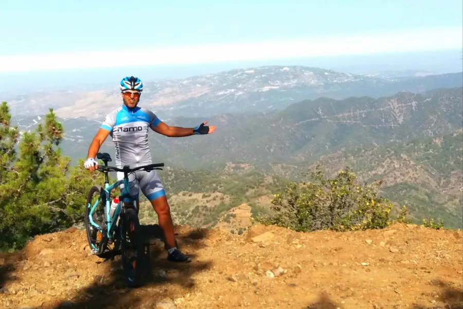 A mountain biker beside the bike on a bare summit, ridges falling away behind