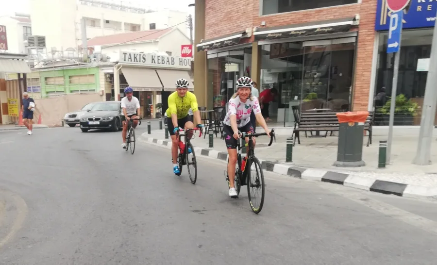 Three riders rolling through a town street past shop fronts and parked cars