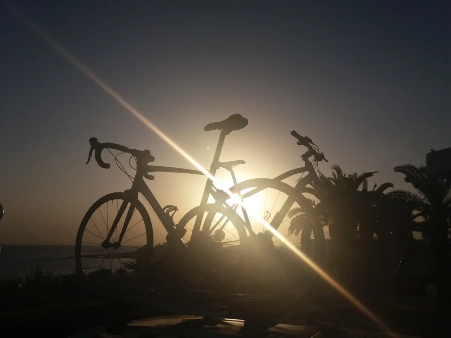 A road bike and a mountain bike on a car roof rack in silhouette against a sunset over the sea