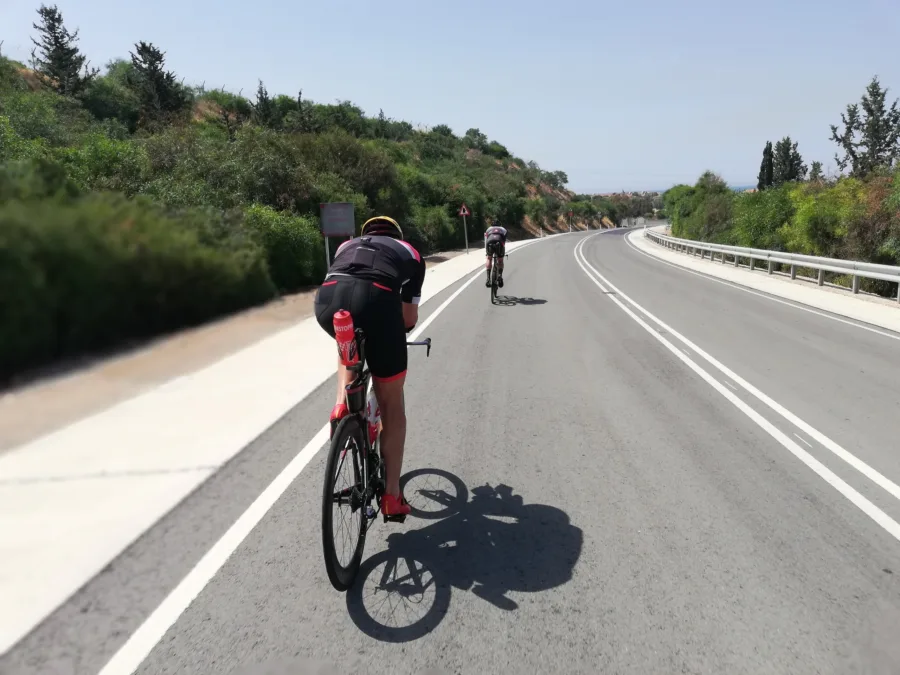 A rider on the tri-bars leading a second rider along a wide open road in bright sun