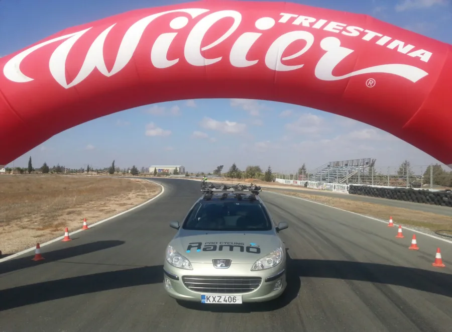The branded car with bikes on the roof, parked under a red inflatable Wilier Triestina arch at a race circuit