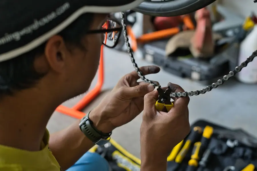 A mechanic in a cap using a chain tool on a bicycle chain, a toolbox open below