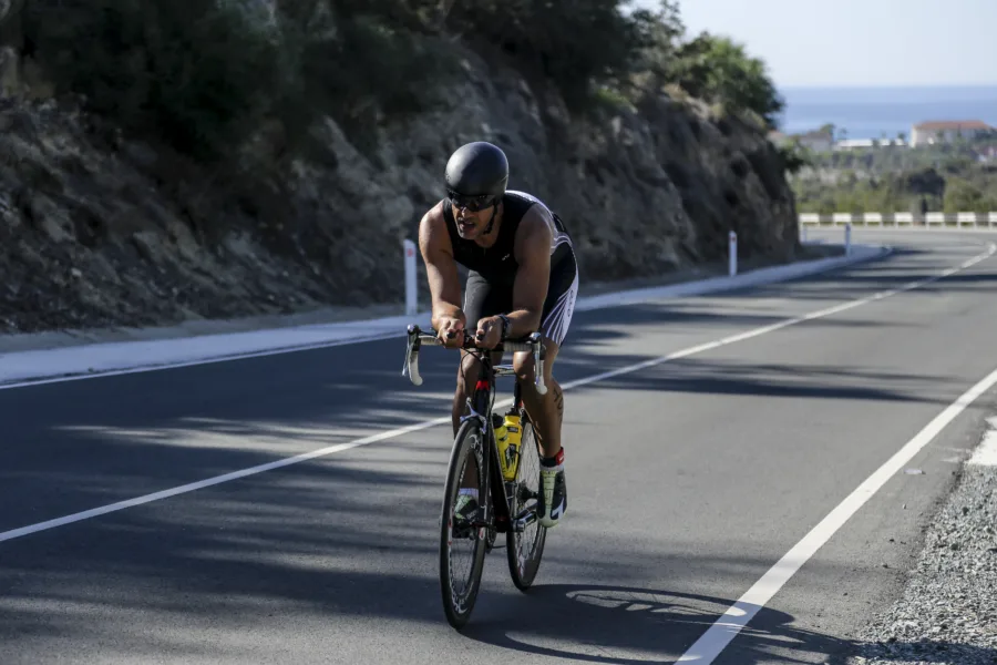 A rider in an aero helmet on a time-trial bike on a wide road cut into a rock face