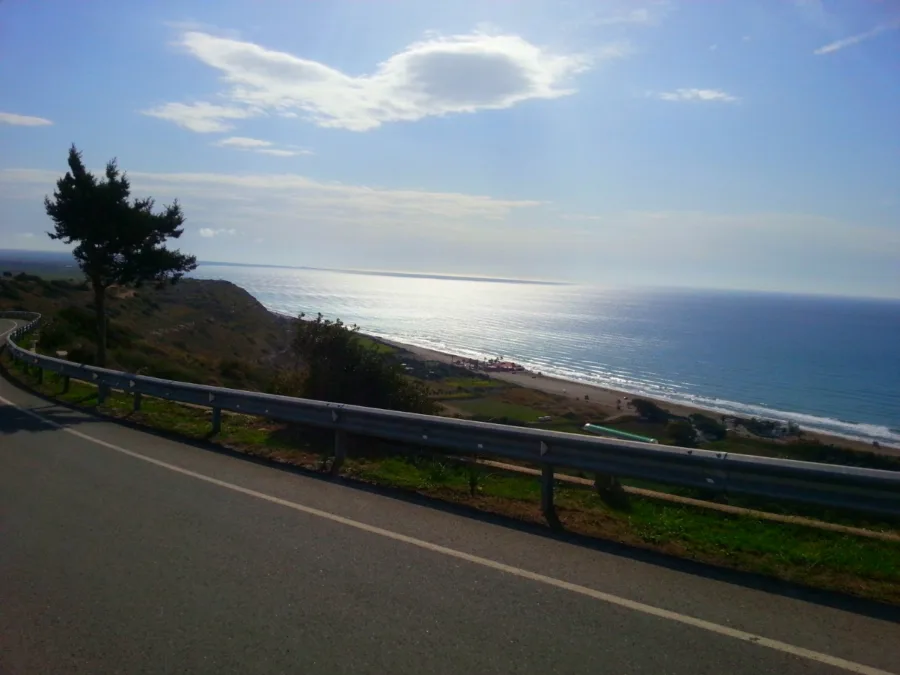 An empty road curving downhill behind a guardrail, the sea filling the horizon beyond