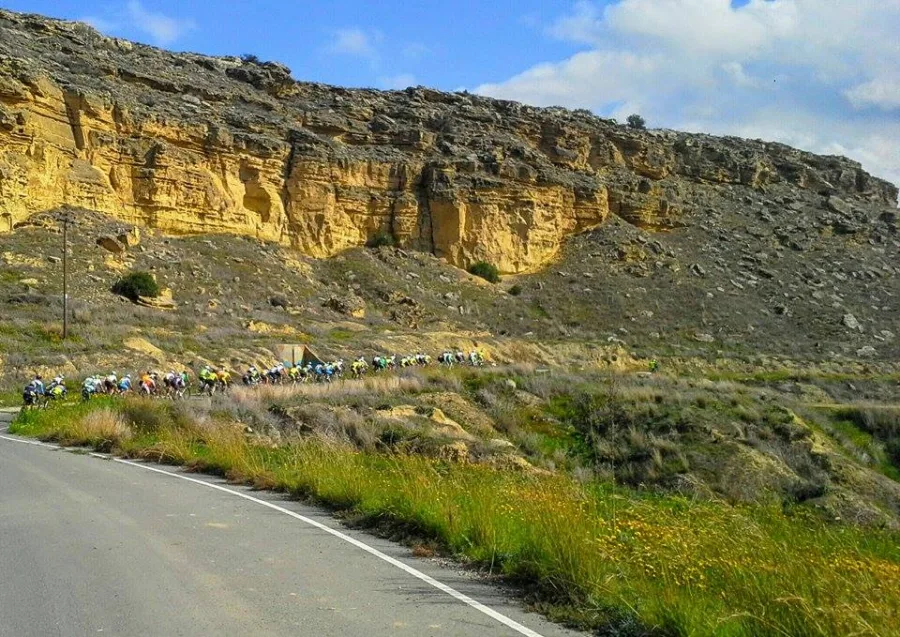 A road running below a layered cliff face with riders in the distance