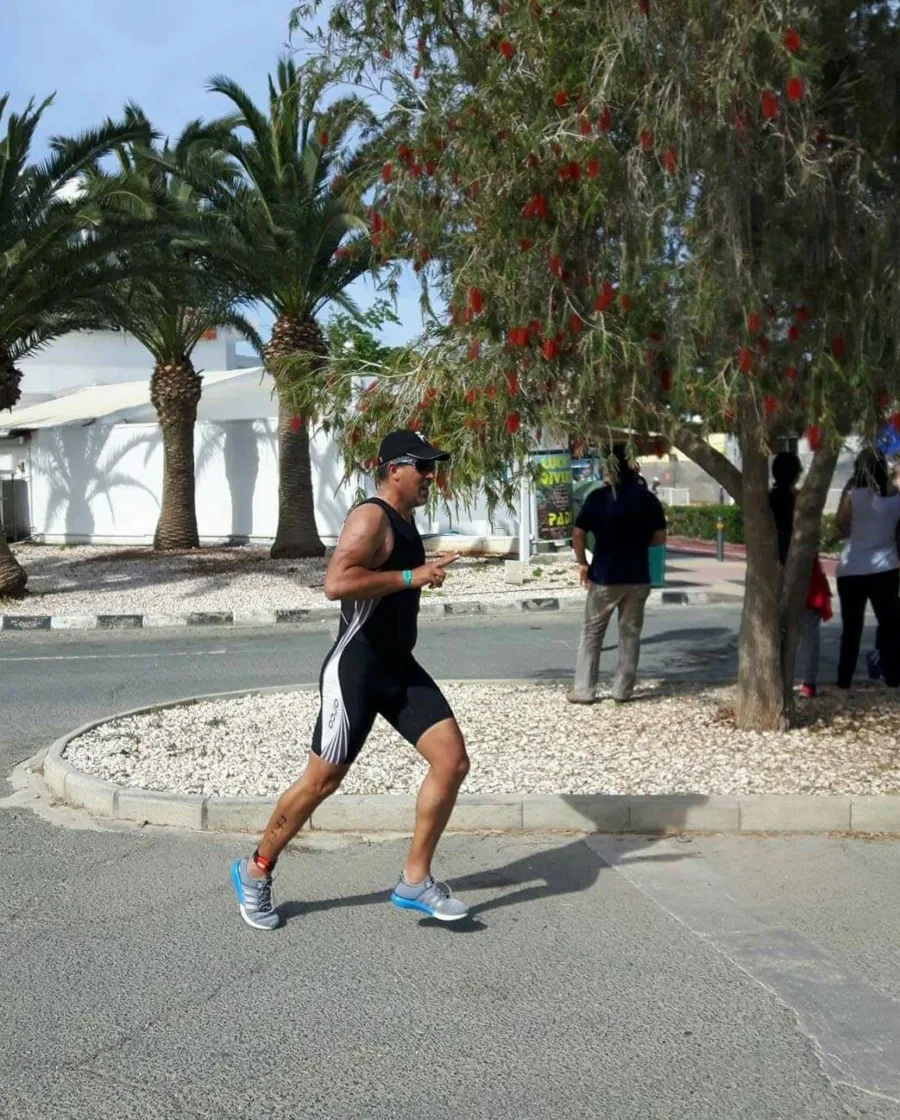A triathlete running along a shaded path in a black tri suit
