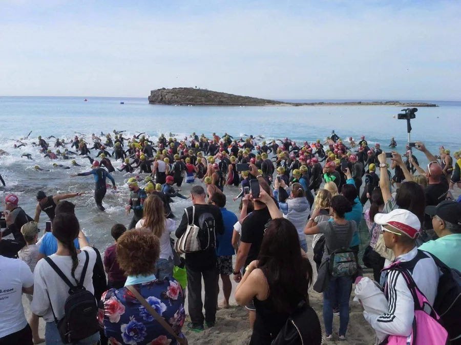 A crowded beach at a triathlon swim start, swimmers wading into the sea