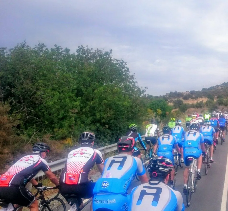 A long line of riders in team kit climbing a road past scrub