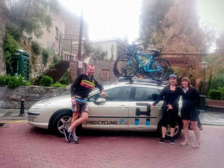 Riders and friends around the Ramo team car on a paved street