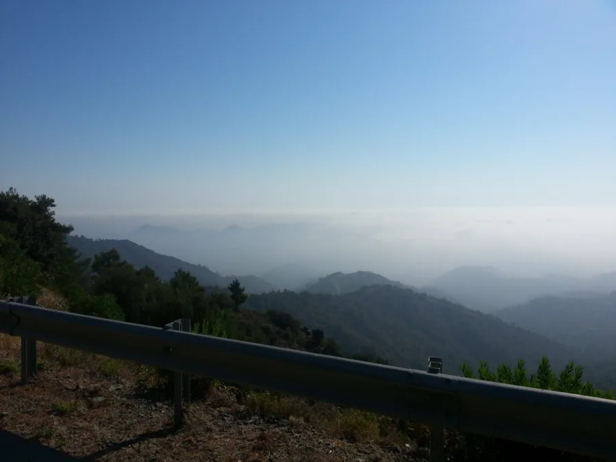 Wooded ridges falling away into haze, seen over a crash barrier from a mountain road