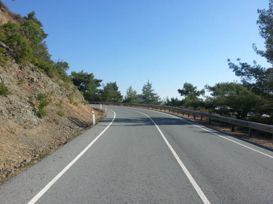 An empty mountain road climbing between pines under a clear sky