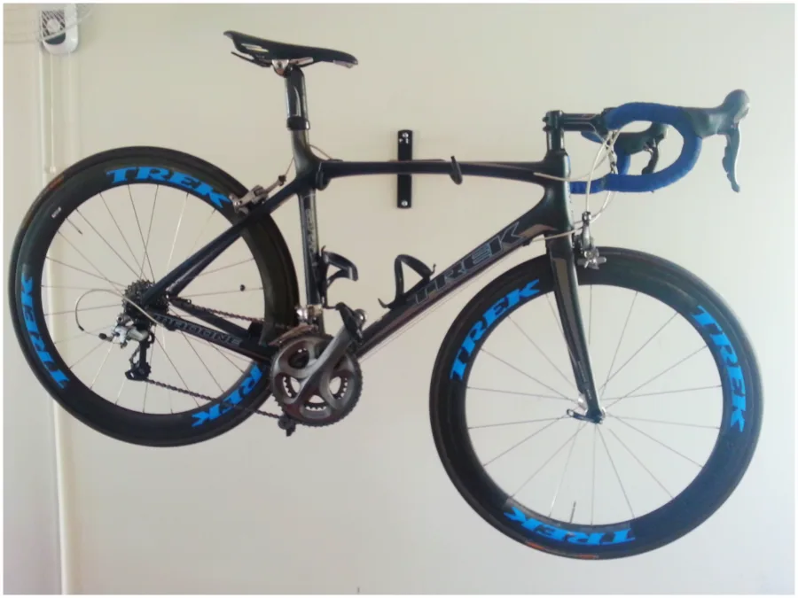 A black carbon road bike with deep-section blue wheels hanging on a white wall