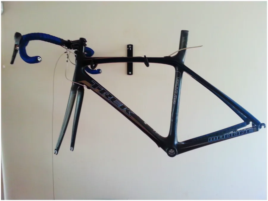 A bare black carbon road frame and fork hanging on a white wall