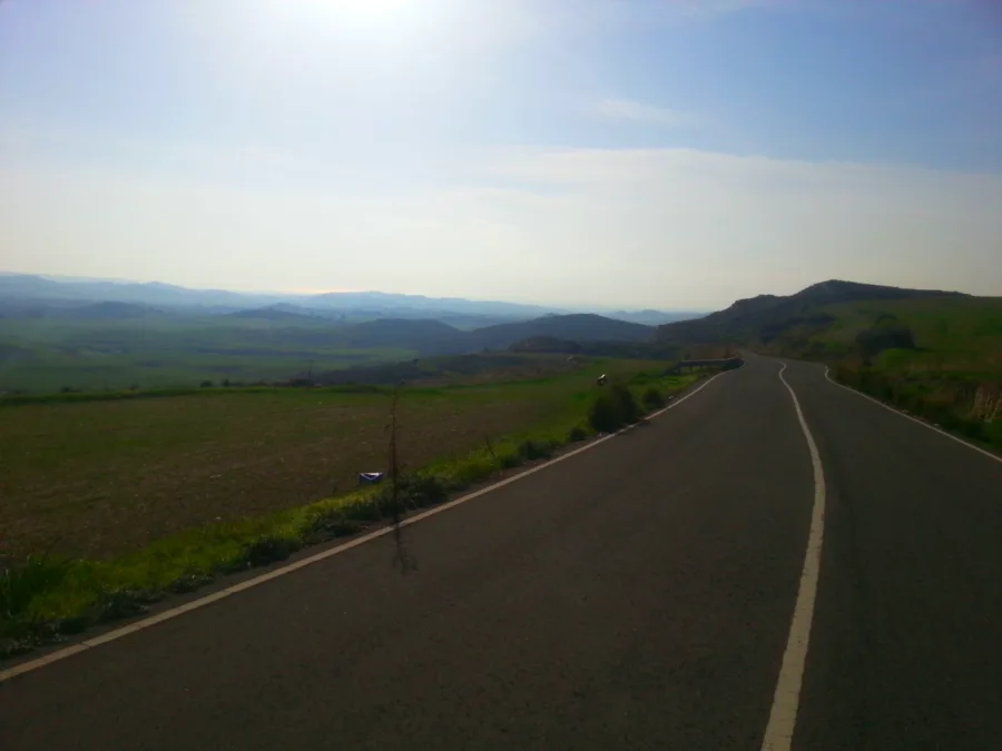 An empty road running straight across open farmland towards low hills