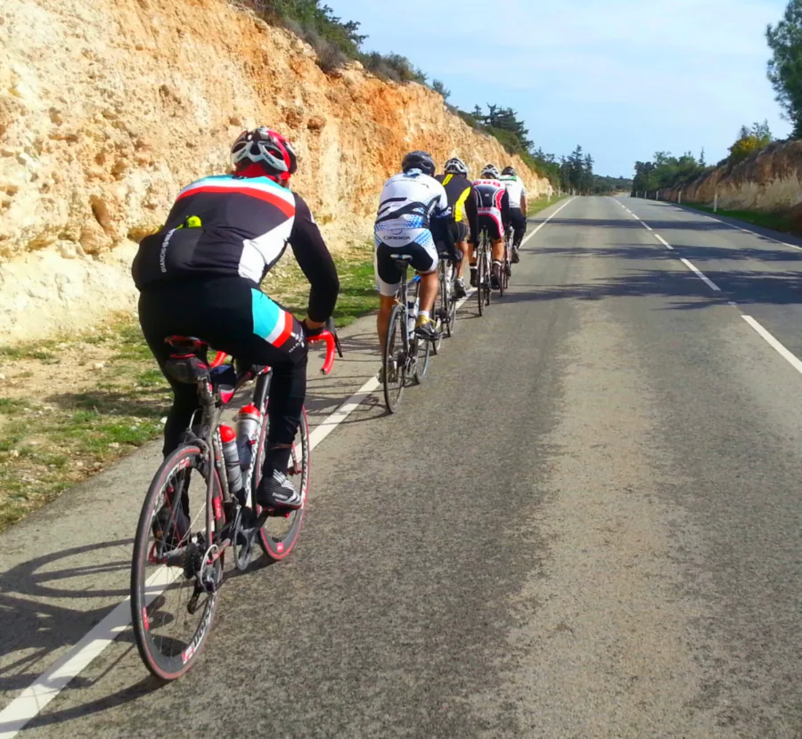 Riders climbing single file past a pale rock cutting on a coast road
